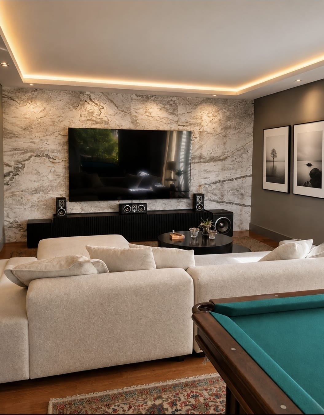 Sala de estar com painel marmorizado, sofá claro e mesa de bilhar.