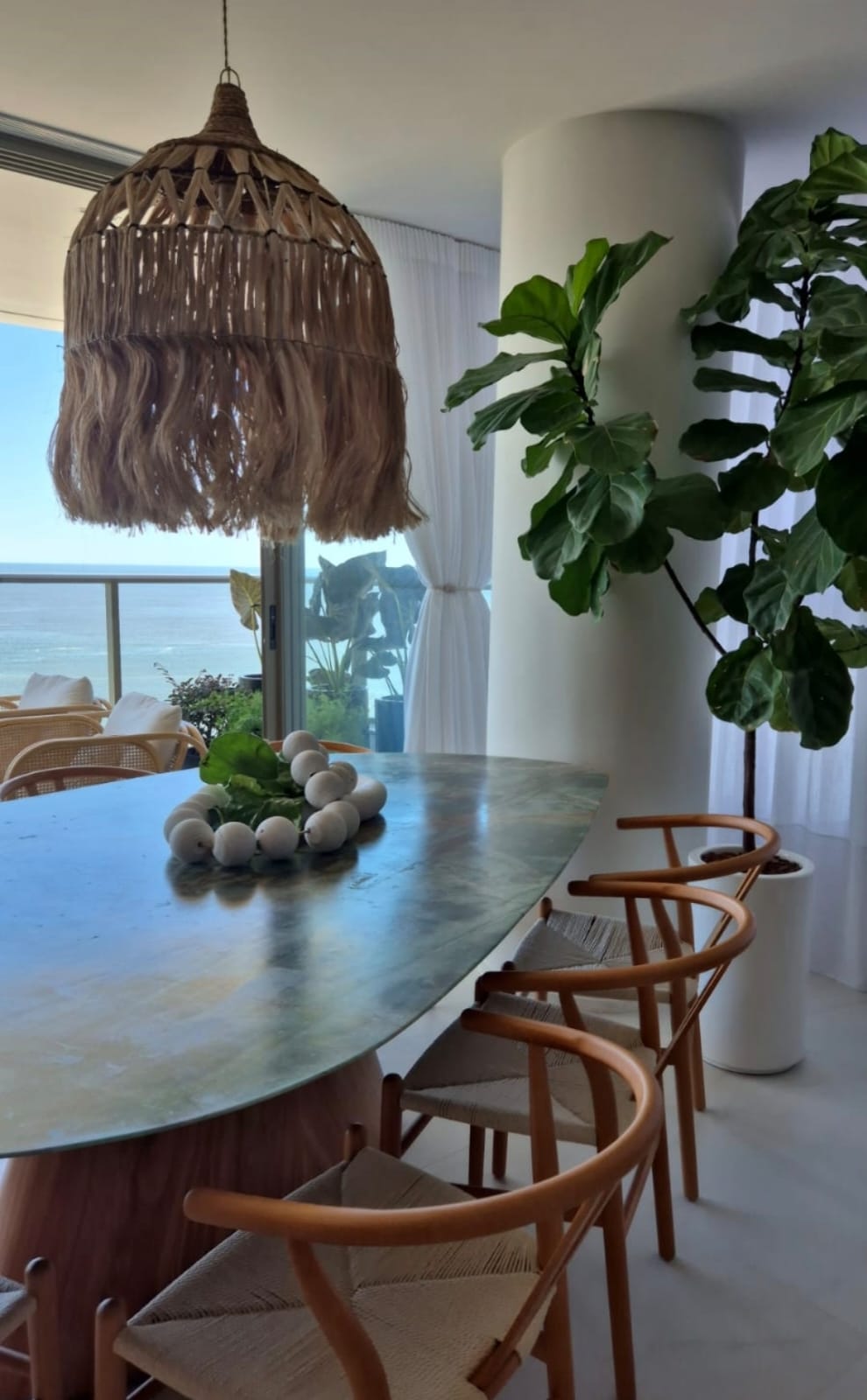 Sala de jantar com mesa oval, cadeiras de madeira e vista para o mar
